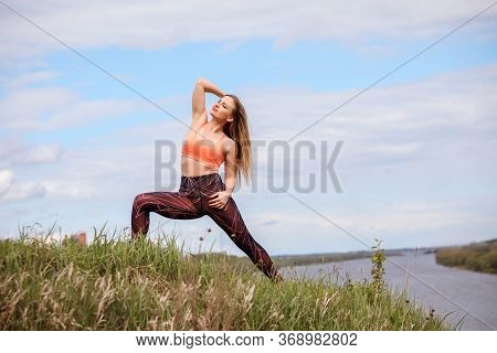 Athletic Woman Is Standing In The Lunge Pose On The Pank Of The River.
