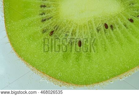 Close-up Of Fresh Kiwi Fruit Slice On Light Background. Slice Of Ripe Green Kiwi Fruit In Sparkling 