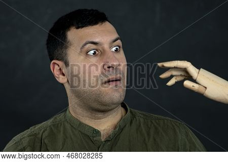 Portrait Of A Surprised Man 30-35 Years Old, Looking At A Wooden Model Of An Attacking Hand. Concept