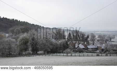 Beautiful Wintry Landscape Of Farm In Fog In English Countryside At Dawn With Hoarfrost Covering Tre