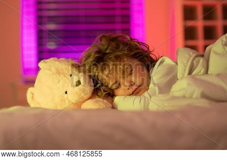 Kid Enjoying Sweet Dreams. Kid Sleeping With A Toy Teddy Bear In Bed. Child Sleeping In Bed Under Bl