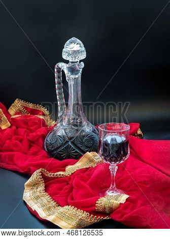 Composition With Red Wine On A Crystal Wineglass With Antique Glass Wine Decanter On Red Silk Sari. 