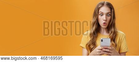Young Girl Shocked Reading Messages In Friends Smartphone Folding Lips Popping Eyes In Amazement At 