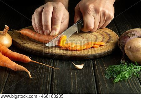 Chef Cuts Fresh Carot On A Wooden Cutting Board. Close-up Of Cook Hands While Preparing Vegetarian F