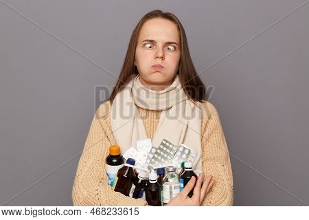 Portrait Of Tired Crazy Caucasian Woman Wearing Jumper And Scarf Holding Pills, Standing Isolated Ov