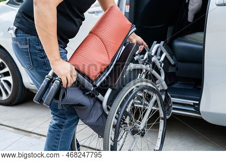 Asian Woman Folding And Lift Up Wheelchair Into Her Car. Accessibility Concept.