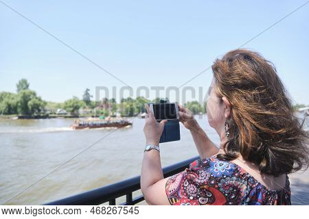 Mature Latin Woman Taking Pictures With Her Phone On The Banks Of The Lujan River In Tigre, Buenos A