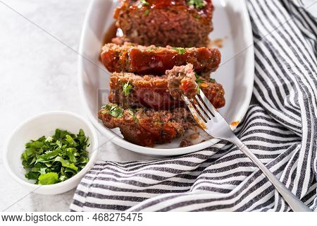 Slicing Classic Meatloaf With A Sweet Glaze On A White Serving Plate