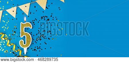 Number 5 Gold Celebration Candle On Star And Glitter Blue Background. Copy Space. Banner