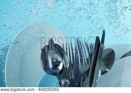 Washing Silver Cutlery And Plates In Water On Light Blue Background