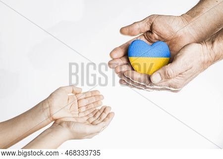 Old Hands Give Painted Yellow And Blue Heart To Chldrens Hands On White Background. Concept Needs He