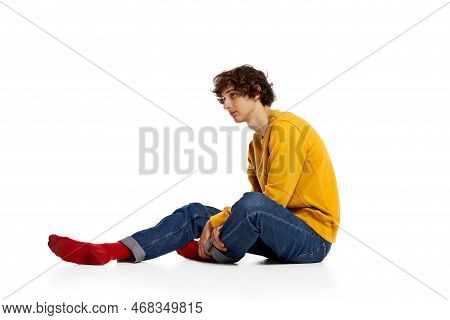 Portrait Of Young Boy Sitting On Floor In Sadness, Feeling Asocial Over White Background. Loneliness