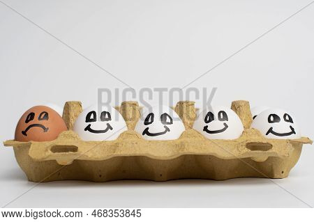 Paper Tray Full Of Smile White Eggs And Only One Different Sad Orange Egg. Discrimination, Xenophobi