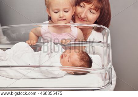 The Sister And Grandmother Looks At A Newborn Baby In The Hospital Ward