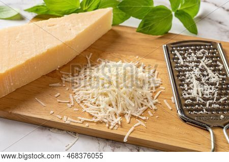Finely Grated Grana Padano Cheese Over Wooden Cutting Board. Parmesan Whole Wedge, Grated Cheese And
