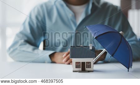 Individuals Holding Small Umbrellas And Model Homes, Housing Insurance Against Impending Loss And Fi
