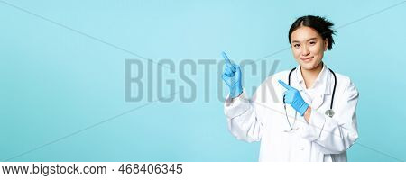 Smiling Female Doctor, Physican In Medical Uniform And Sterile Gloves, Pointing Fingers Left At Prom