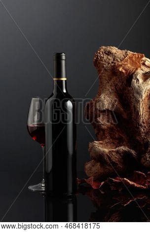 Bottle And Glass Of Red Wine. In The Background Old Driftwood And Dried-up Vine Leaves. Frontal View