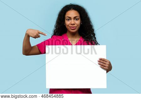 Dark-skinned Female Nurse In Pink Uniform Holds Horizontal Banner Blank Ad Space On Blue Background.