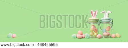 Easter Bunny Ears And Feet Two Sweets Jars With Many Tiny Eggs In And Near On Green Edgeless Backgro