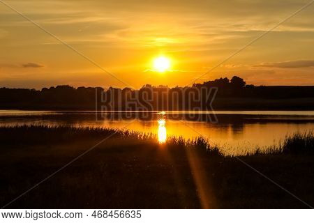 Beautiful, Golden Sunset Sunrise Over A Lake. Crepuscular Rays And Clouds Reflected In Calm Water.