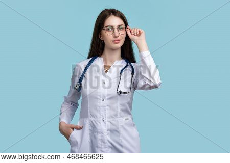 Female Ophthalmologist In Round Eyewear Posing On Blue Background Studio. Intern Doctor General Prac