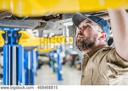 Closeup Of Caucasian Middle Aged Mechanic Inspecting Undercarriage Of The Vehicle Secured On Car Lif