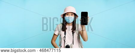 Enthusiastic Young Asian Woman In Medical Face Mask, Showing Mobile Phone App Interface, Tourism App
