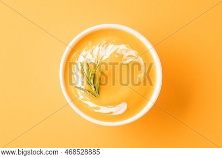 Thick Butternut Squash Bisque In White Bowl Garnished With Heavy Cream And Rosemary Over Orange Back