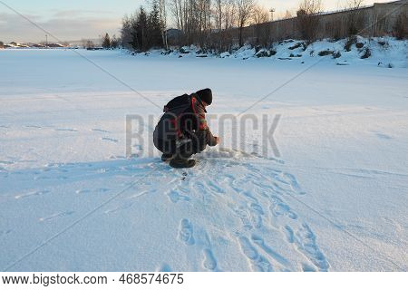 Fisherman On Winter Fishing. A Man Sits Near A Hole In A Frozen Lake Waiting For A Bite. Snow On Ice