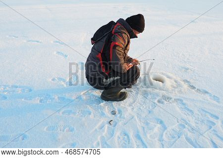 Fisherman On Winter Fishing. A Man Sits Near A Hole In A Frozen Lake Waiting For A Bite. Snow On Ice