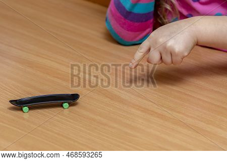 A Child\'s Hand Rolls A Fingerboard Against The Background Of A Wooden Surface, Close-up, Selective 