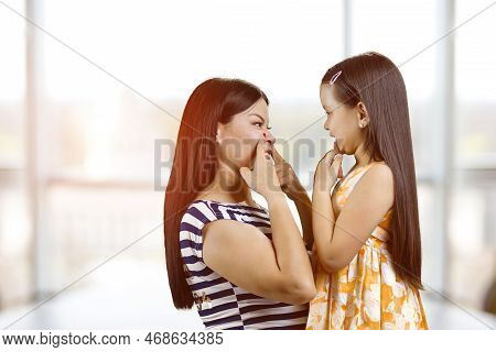 Woman And Little Girl Are Having Fun Making Faces To Each Other. Indoor Windows Background.