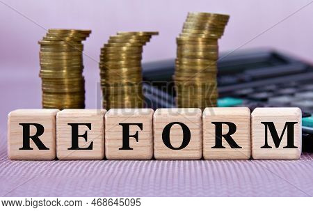 Reform - Word On Wooden Cubes On The Background Of Coins And Calculator. Business And Finance Concep