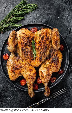 Tobacco Whole Chicken On Plate With Herbs And Tomato. Black Background. Top View.