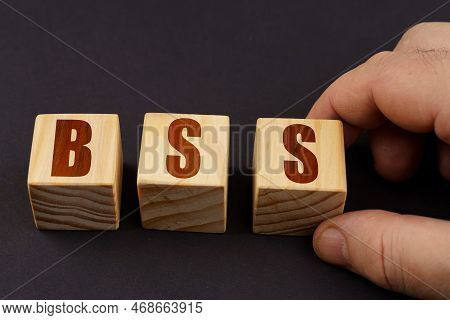 Business Concept. On A Black Surface, A Man Puts Cubes With The Inscription - Bss