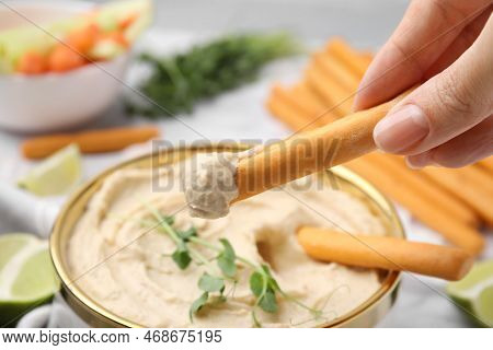 Woman Dipping Grissini Stick Into Hummus At Table, Closeup