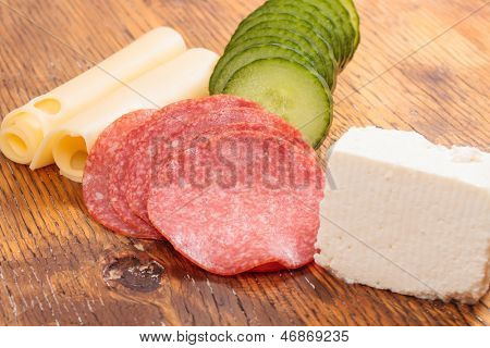 Feta und Ementhal Käse mit Salami und Gurken auf einer Holzplatte