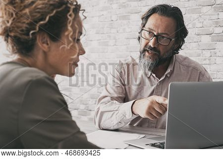 One Man Explain Concept At Work To A Woman Sitting At The Desk. Business Couple At Office Using Lapt