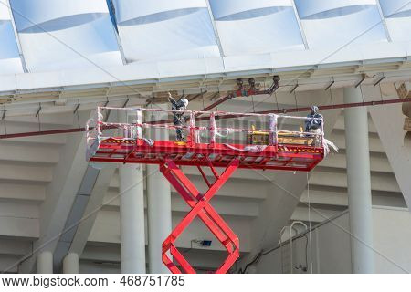Construction Workers Standing In The Scissors Lifting Crane Bucket While Working At High Level In Th