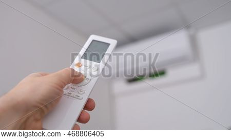 Woman Hand Holds Remote Control Pointing At Air Conditioner In Room. Adjusted To Ambient Temperature