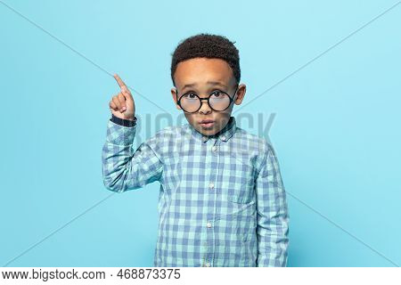 Look Here. Little Black Boy In Eyeglasses Pointing Aside, Showing Free Space For Ad, Looking At Came