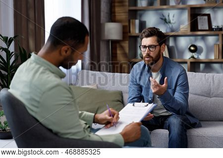 Visit To A Psychologist. A Man Sits On A Couch And Talks To A Psychotherapist. The Patient Is Depres