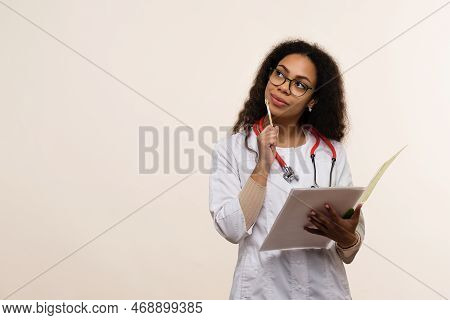 Dark Skinned Female Doctor In Uniform With Eyeglasses And Stethoscope On Light Background In Studio.