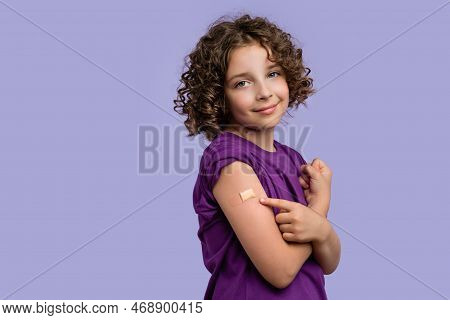Portrait Girl 10-12s In Violet T-shirt Showing Arm After Coronavirus Vaccination On Lilac Studio Wal