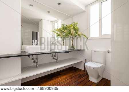 Two Square Sinks On Black Marble Countertop In Spacious Bathroom With Window To Street. Large Mirror