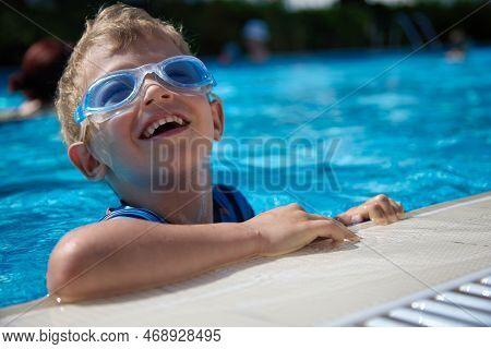 Boy Cheerfully Swims In The Childrens Pool, Dives In Swimming Glasses. Summer Entertainment Of A Hap