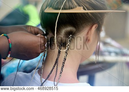 Close-up Of The Masters Hand With A Colored Bracelet That Neatly Weaves Thin Long Pigtails To A Sitt