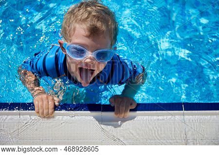 View From Above Of A Boy Sticking Out His Tongue Floating In A Deep Pool Of Clear Water In The Summe