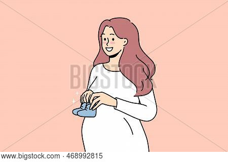 Smiling Young Pregnant Woman Holding Baby Shoes In Hands Excited About Motherhood. Happy Future Moth